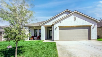 A single-story house with a garage, a small porch with red chairs, and a well-maintained lawn.