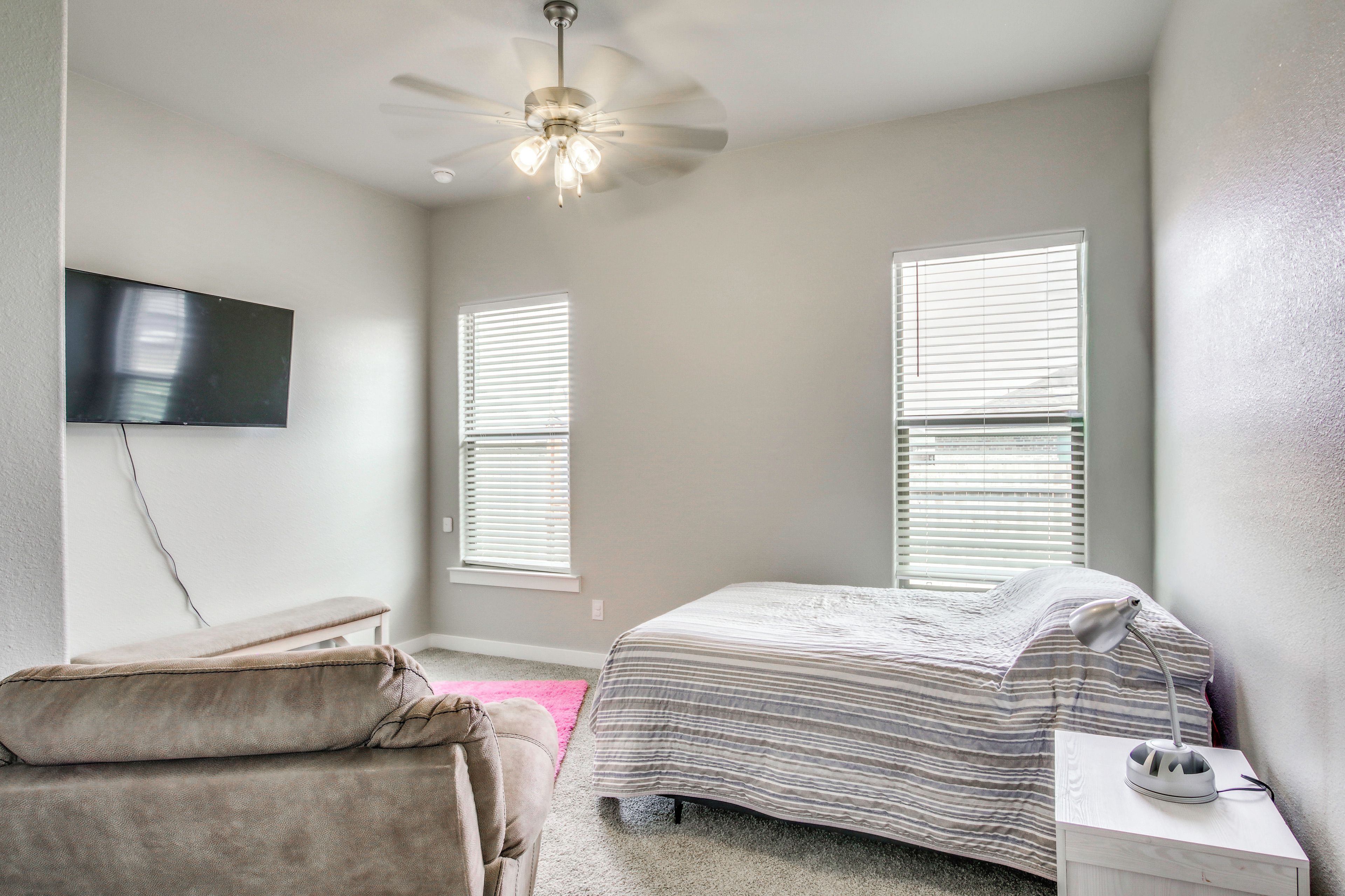 A bedroom with a bed, a bench, a desk, a ceiling fan, and a TV mounted on the wall.