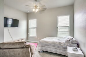 A bedroom with a bed, a bench, a desk, a ceiling fan, and a TV mounted on the wall.