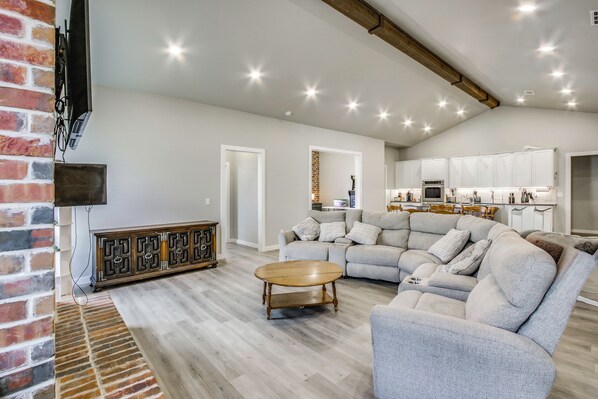 A spacious living area with a large grey sectional sofa, a wooden coffee table, and a brick accent wall.