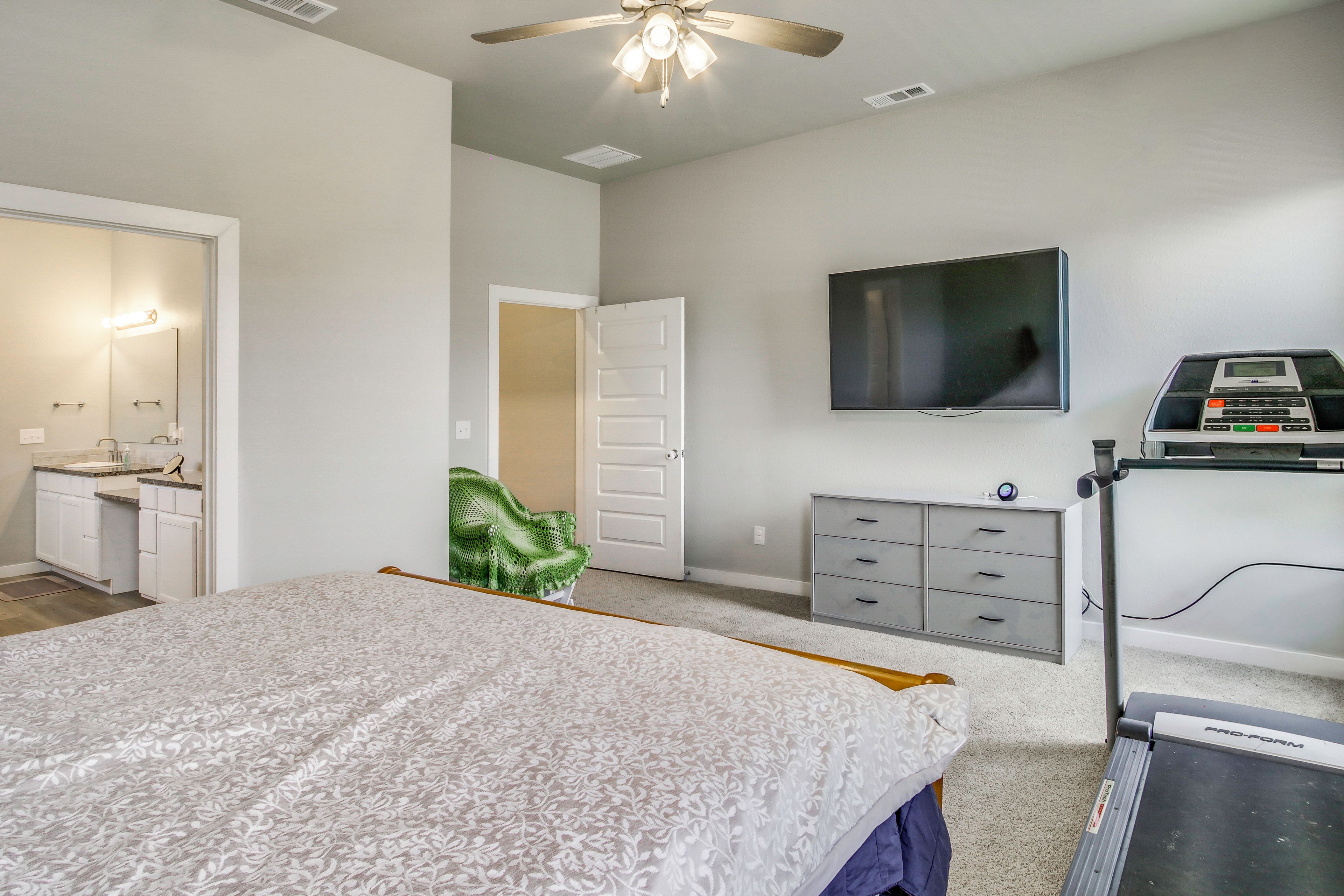 A bedroom with a bed, a television, a treadmill, and a bathroom with a sink and mirror.