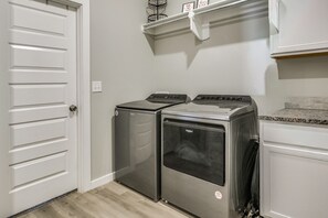 A laundry room with two front-loading washers and dryers, a white door, and a countertop with a sink.
