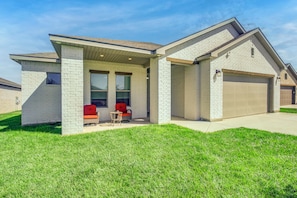 A residential house with a garage, a covered porch with two chairs, and a well-maintained lawn.