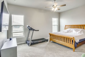 A bedroom with a bed, a treadmill, a desk, and a ceiling fan.