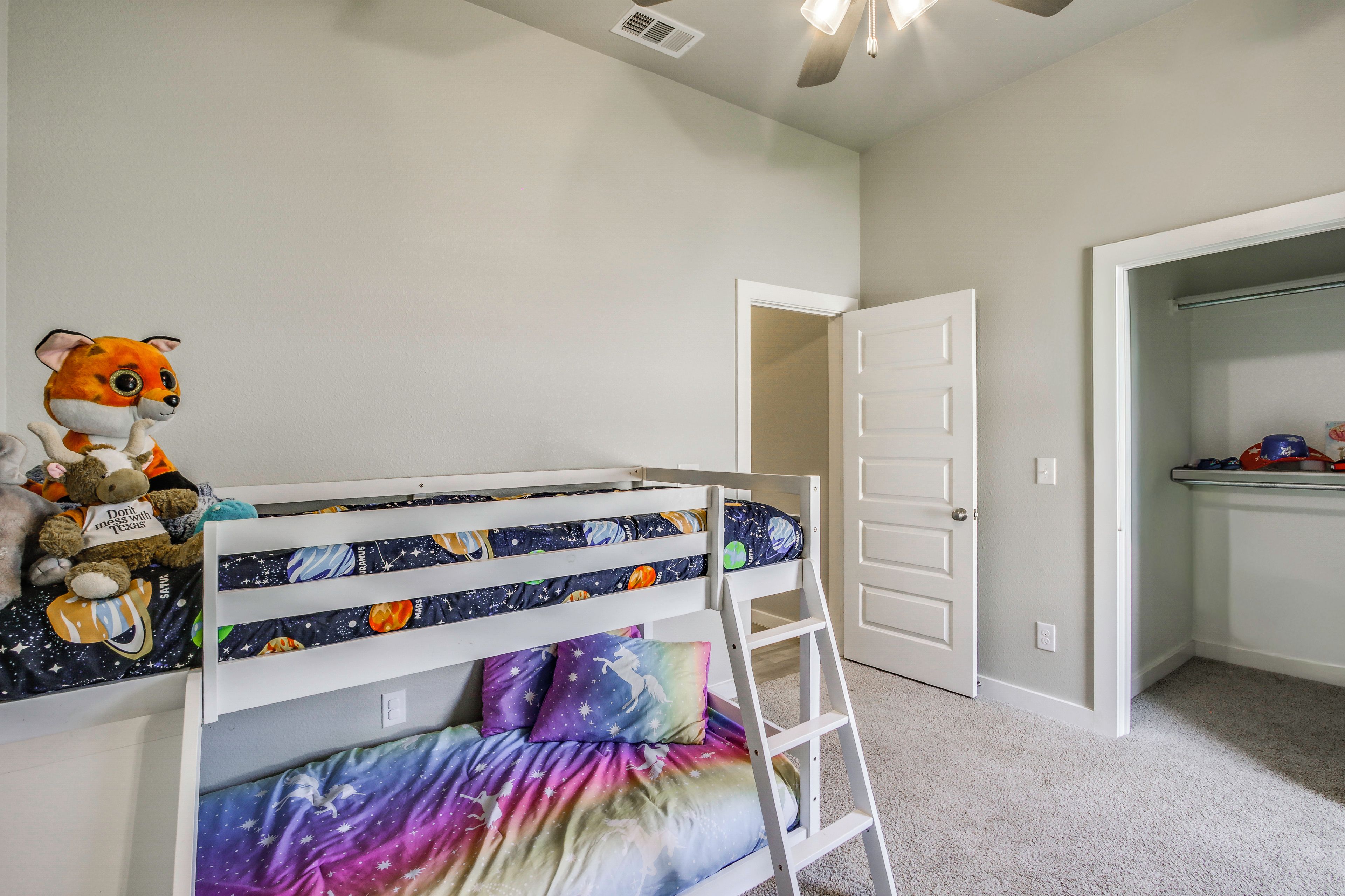 A child's bunk bed with space-themed bedding, a ladder, and a stuffed toy on the bed.