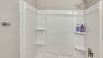 A corner of a bathroom with a shower, a toilet, and a shelf with toiletries.