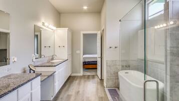 A modern bathroom with a walk-in shower, a large bathtub, and a vanity with a mirror and lights.
