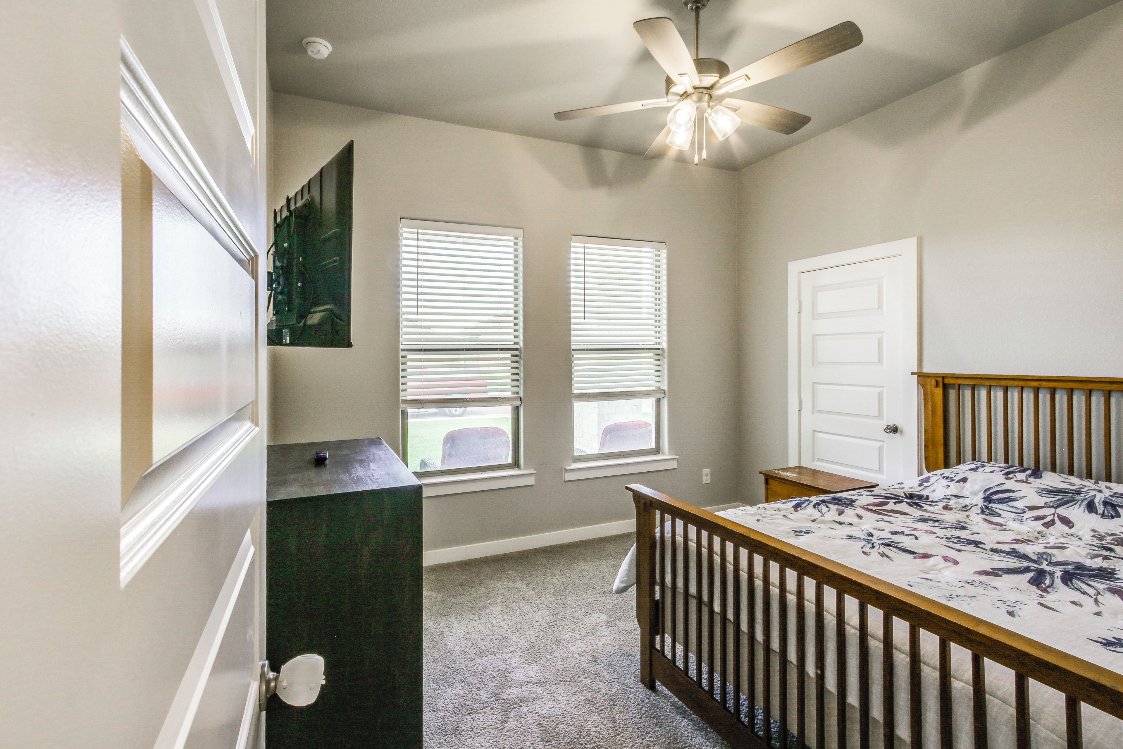 A bedroom with a crib, two windows with blinds, a ceiling fan, and a door.