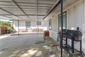 Ein überdachter Patio-Bereich mit Grill, Bank und Gartenmöbeln.