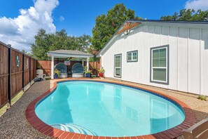 A backyard with a swimming pool, a covered patio, and a wooden fence.
