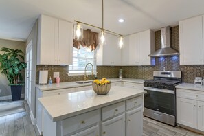 A modern kitchen with white cabinetry, a stainless steel stove, and a center island with a bowl of lemons.