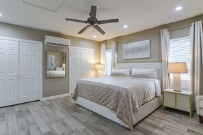 A bedroom with a bed, a ceiling fan, a bedside lamp, a window with curtains, and a wall-mounted mirror.
