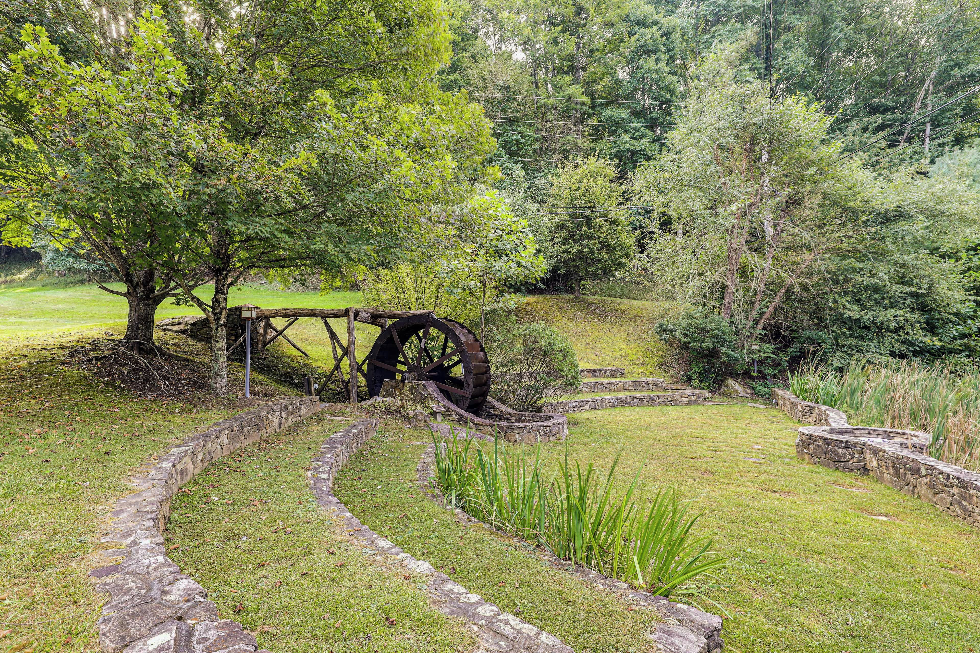 A stone pathway leading through a grassy area with a large water wheel and a wooden fence.