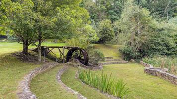 A stone pathway leading through a grassy area with a large water wheel and a wooden fence.
