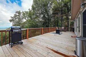 A wooden deck with a barbecue grill, outdoor furniture, and a view of trees and mountains.