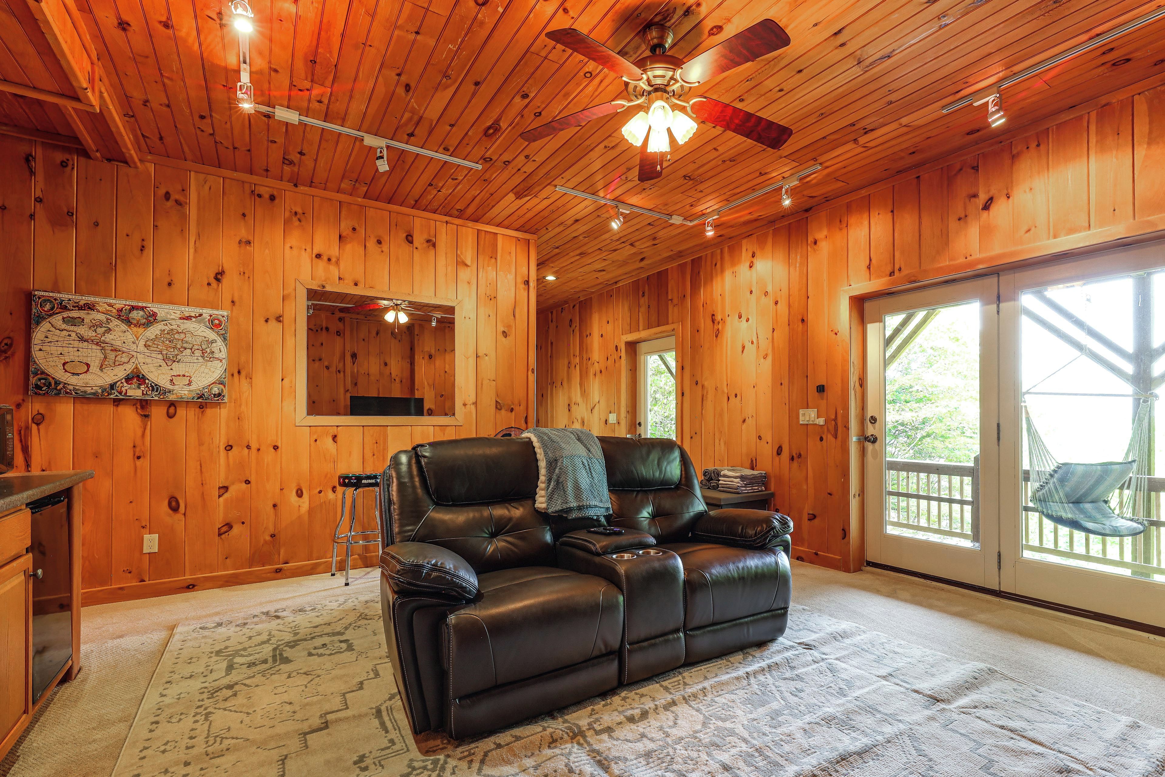 A wooden interior with a leather sofa, ceiling fan, and a large window.