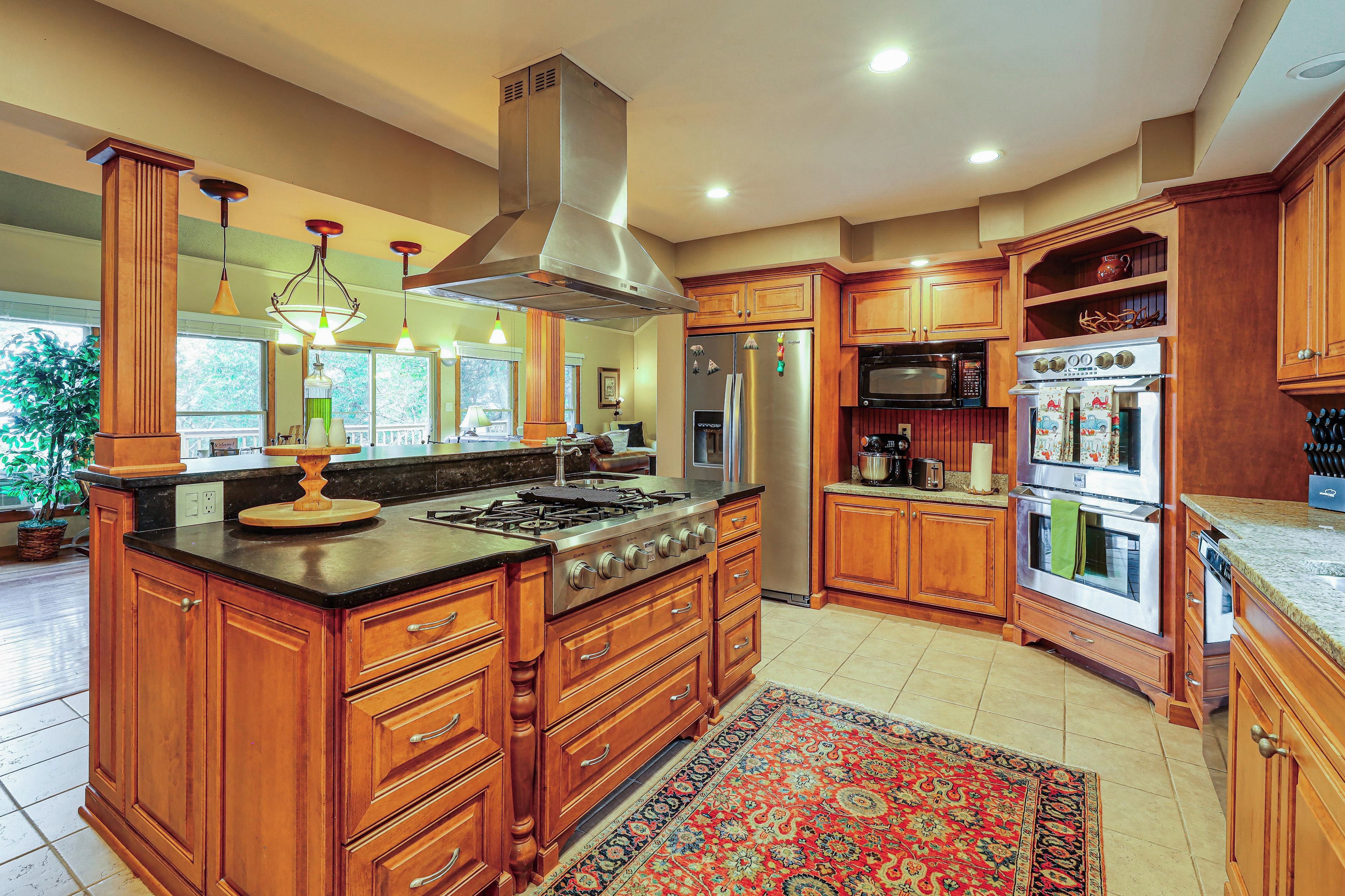 A spacious kitchen with a large island, stainless steel appliances, wooden cabinetry, and a decorative rug.
