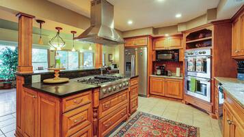 A spacious kitchen with a large island, stainless steel appliances, wooden cabinetry, and a decorative rug.