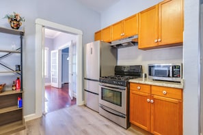 A kitchen with wooden cabinets, a stainless steel refrigerator, a stove, and a microwave. - Quaint North Campus Bungalow Minutes From Downtown (Austin)