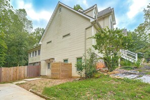 A two-story house with a sloped roof, a wooden fence, and a garden with grass and shrubs. - Wooded Extended Retreat: 15 Mi to Lake Lanier! (Cumming)