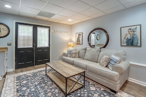 A living room with a sofa, coffee table, patterned rug, wall-mounted clock, and artwork. - Wooded Extended Retreat: 15 Mi to Lake Lanier! (Cumming)