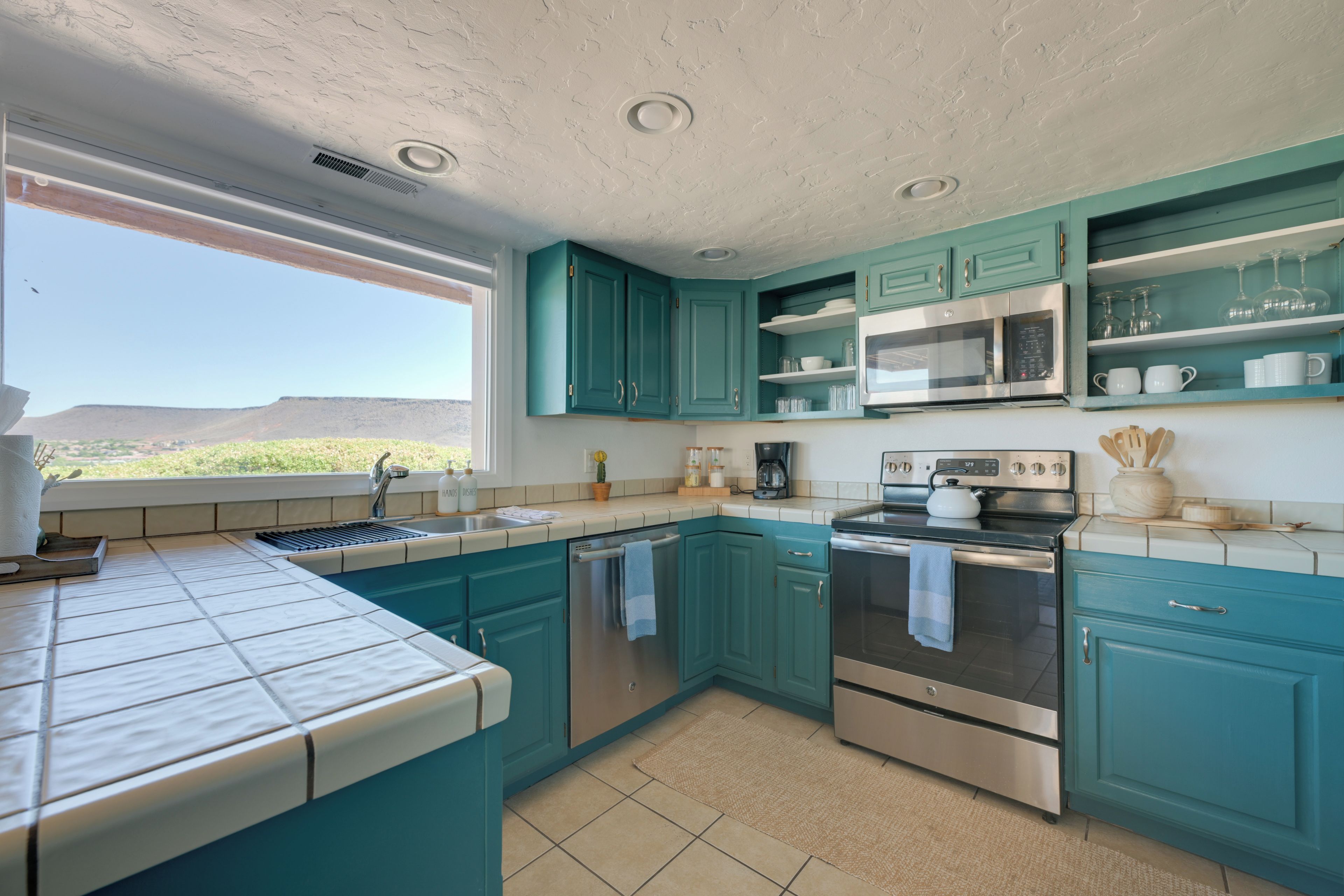 Una cocina con armarios color turquesa, electrodomésticos de acero inoxidable y vistas al paisaje desértico.