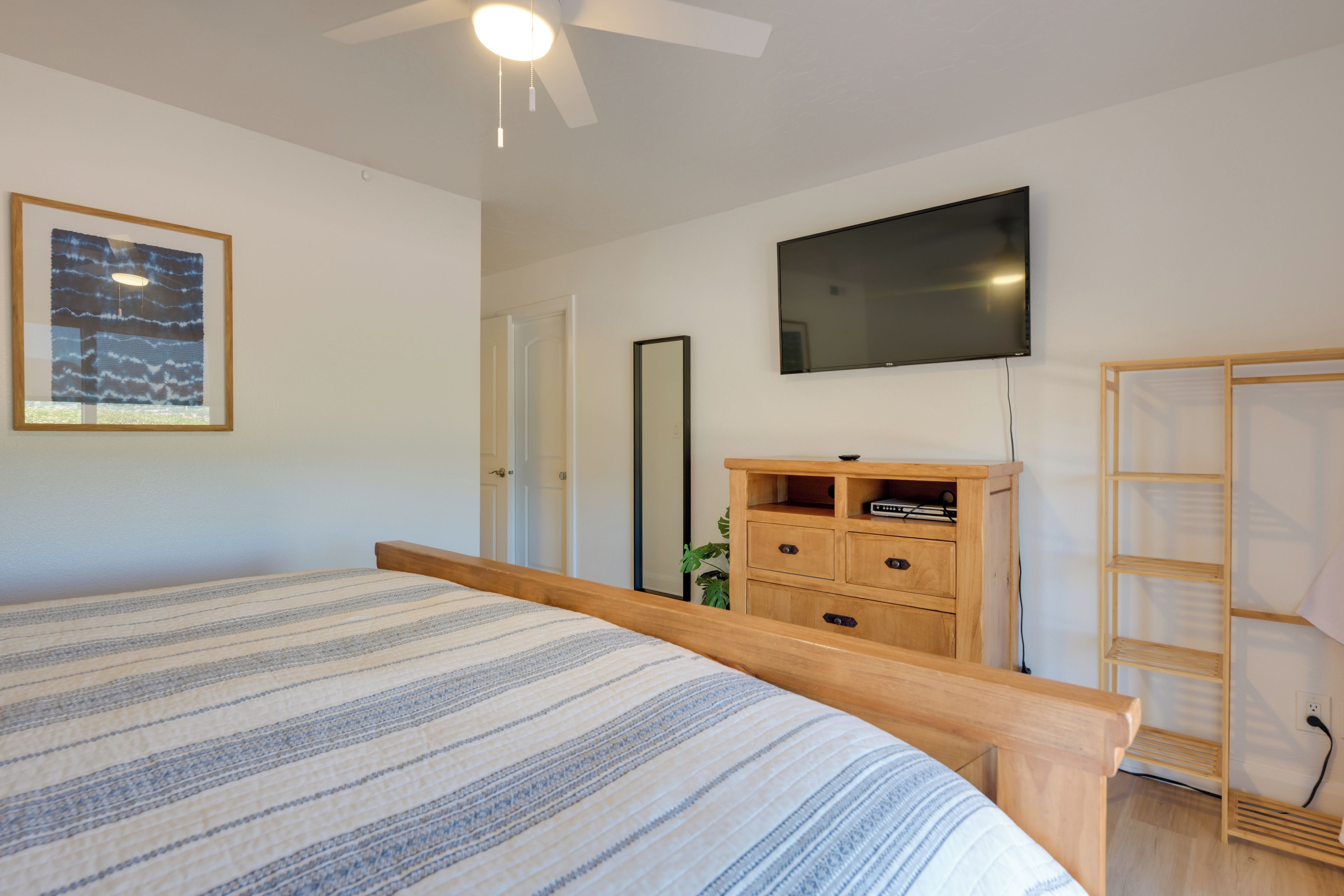 A bedroom with a bed, a TV mounted on the wall, a wooden dresser, and a wardrobe.