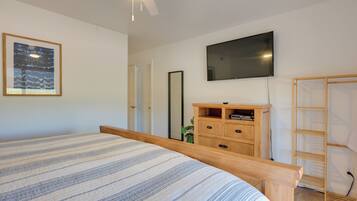 A bedroom with a bed, a TV mounted on the wall, a wooden dresser, and a wardrobe.
