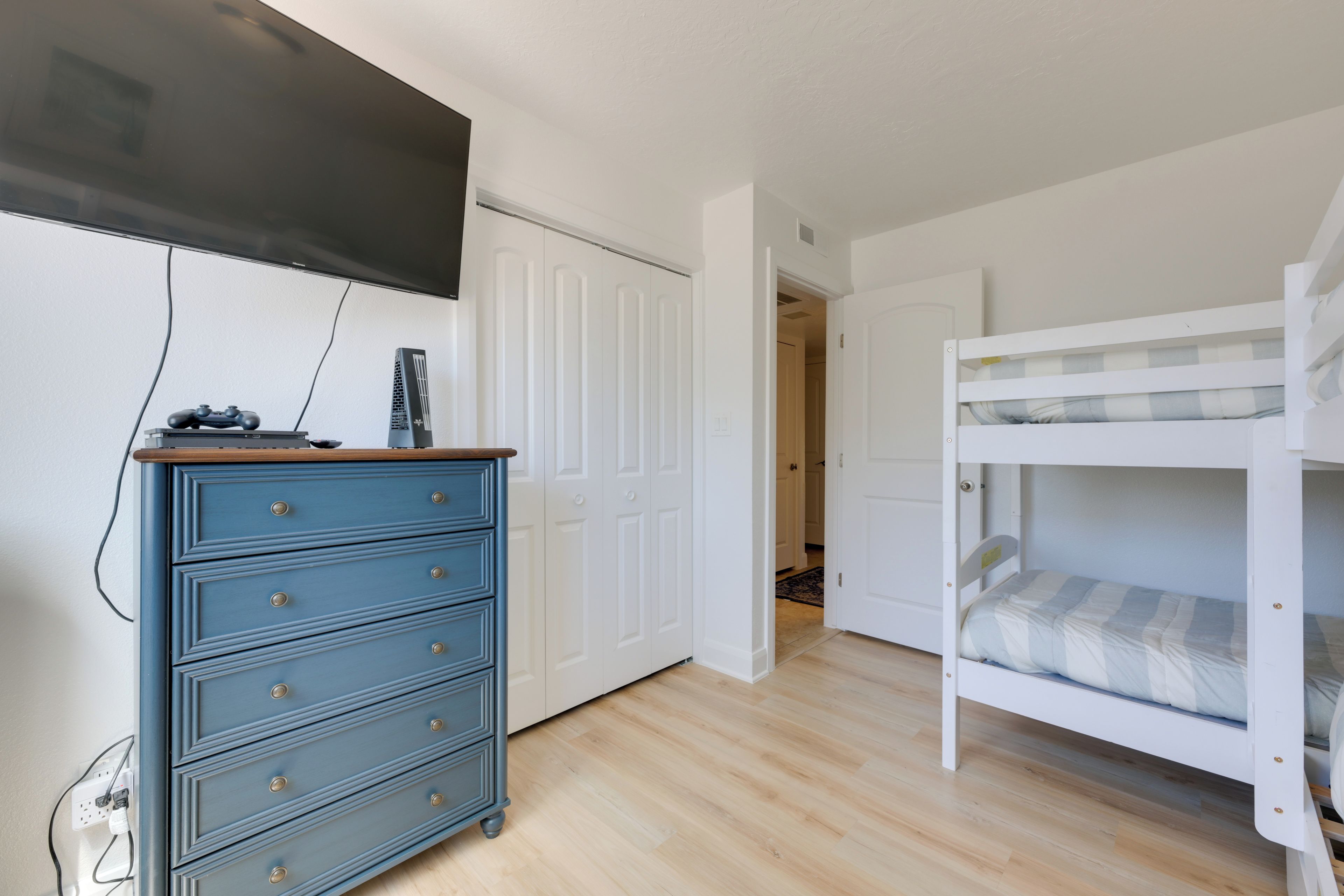 Um quarto com uma cama beliche, cômoda e televisão fixada na parede.