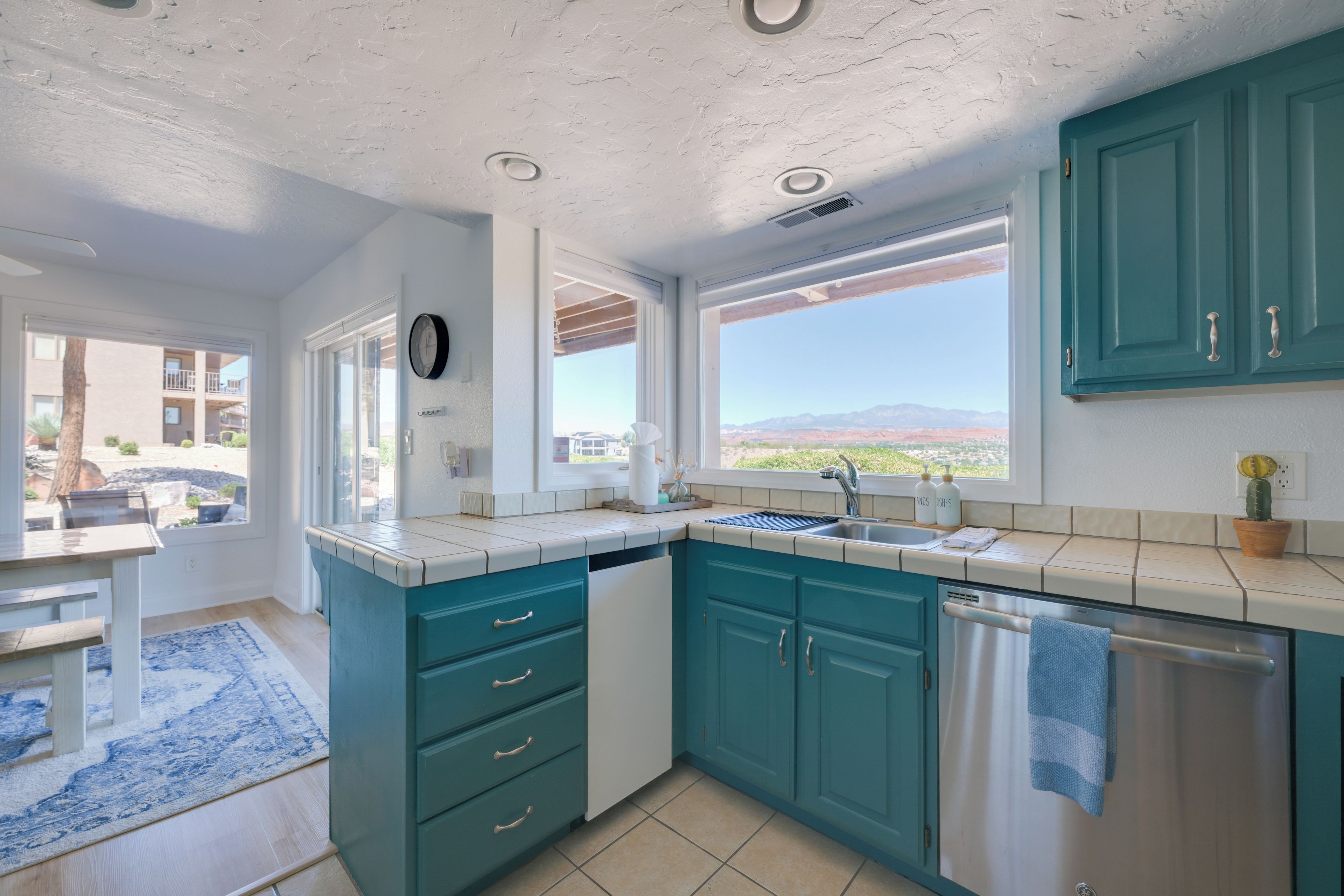 A kitchen with teal cabinets, a sink, and a window with a view of mountains.