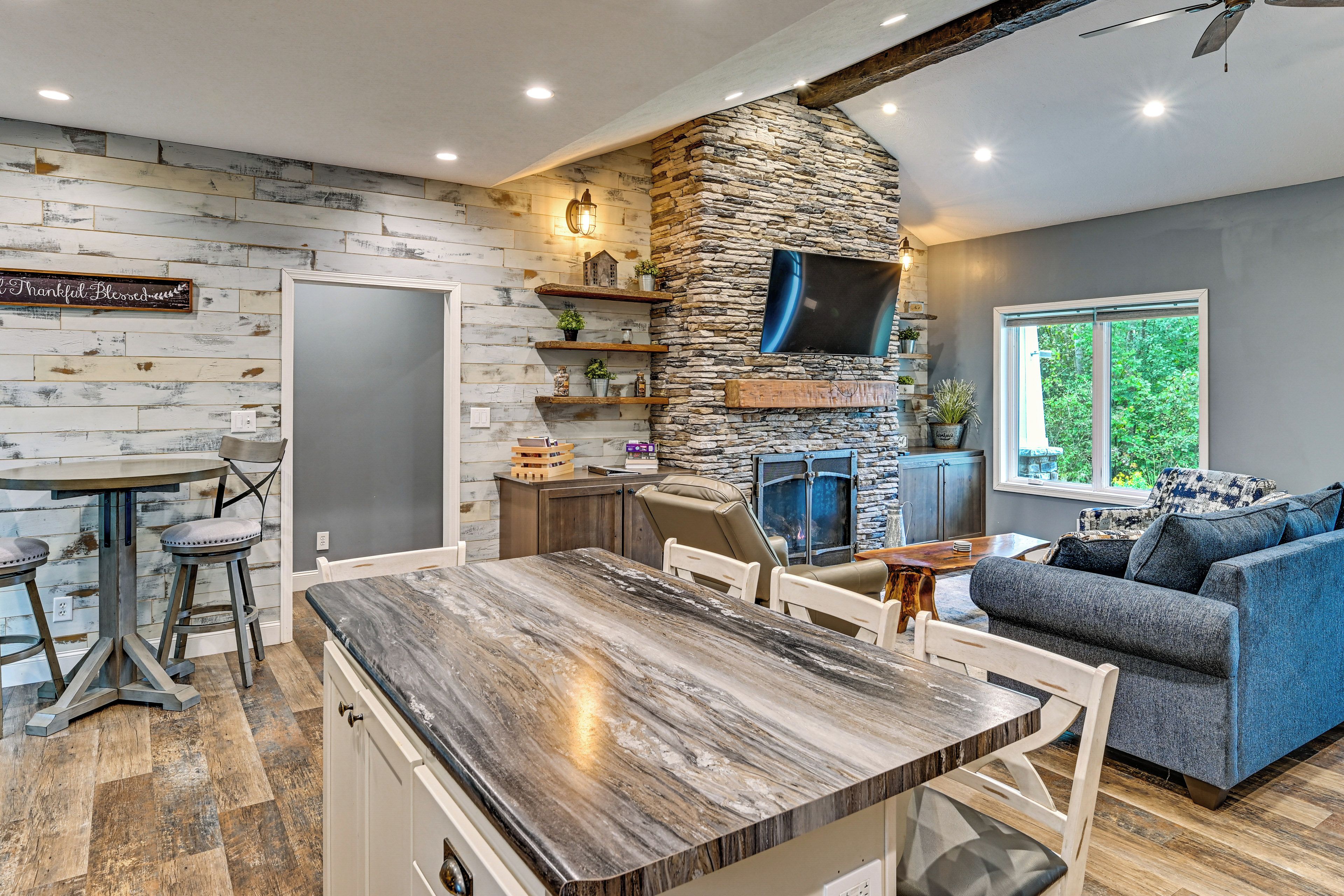 A modern kitchen with a stone accent wall, a dining area with a wooden table, and a living room with a blue sofa.
