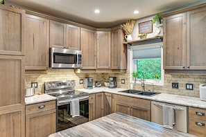A modern kitchen with wooden cabinets, stainless steel appliances, and a marble countertop. - Hot Tub, Game Room & Steps to Pond! Elkhart Escape (Elkhart)