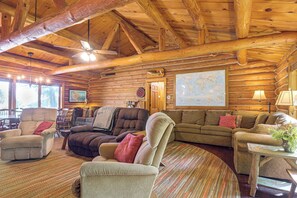 Ein Holzblockhaus-Interieur mit einer gemütlichen Wohnbereitschaft, die einen Kamin, bequeme Sitzgelegenheiten und eine große Weltkarte an der Wand umfasst.