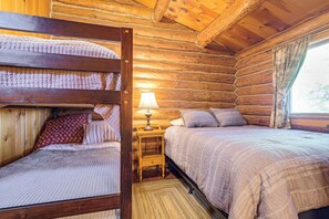A log cabin bedroom with two beds, a nightstand, and a lamp. - North Woods Log House w/ Exceptional Privacy! (Stone Lake)