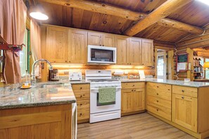 A wooden cabin-style kitchen with a built-in microwave, stove, and granite countertops. - North Woods Log House w/ Exceptional Privacy! (Stone Lake)