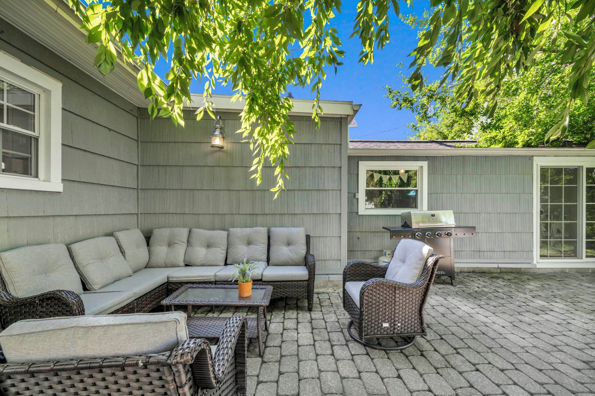 An outdoor patio with a sectional sofa, wicker chairs, a table, and a grill.