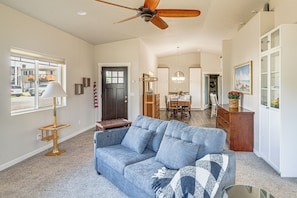 A spacious living room with a ceiling fan, a large window, and a view of the outside. - Holiday at Alsea Bay: 1 Block to the Bay! (Waldport)