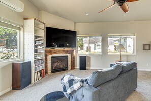 A living room with a fireplace, a television, a bookshelf, and a sofa. - Holiday at Alsea Bay: 1 Block to the Bay! (Waldport)