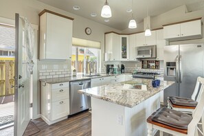 A modern kitchen with white cabinetry, a central island, stainless steel appliances, and pendant lighting. - Holiday at Alsea Bay: 1 Block to the Bay! (Waldport)