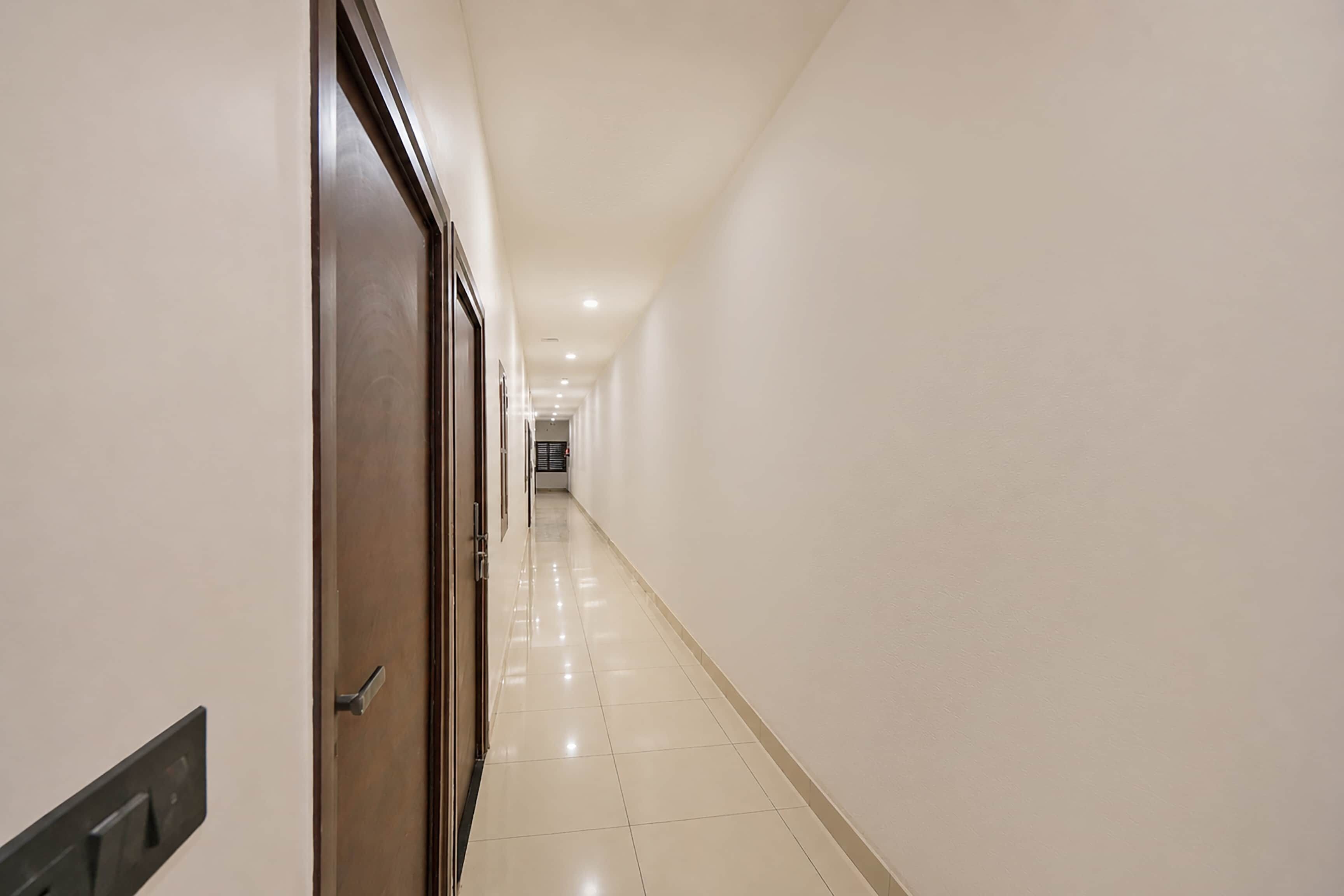 Um corredor com uma porta à esquerda, piso ladrilhado e teto com iluminação embutida.
