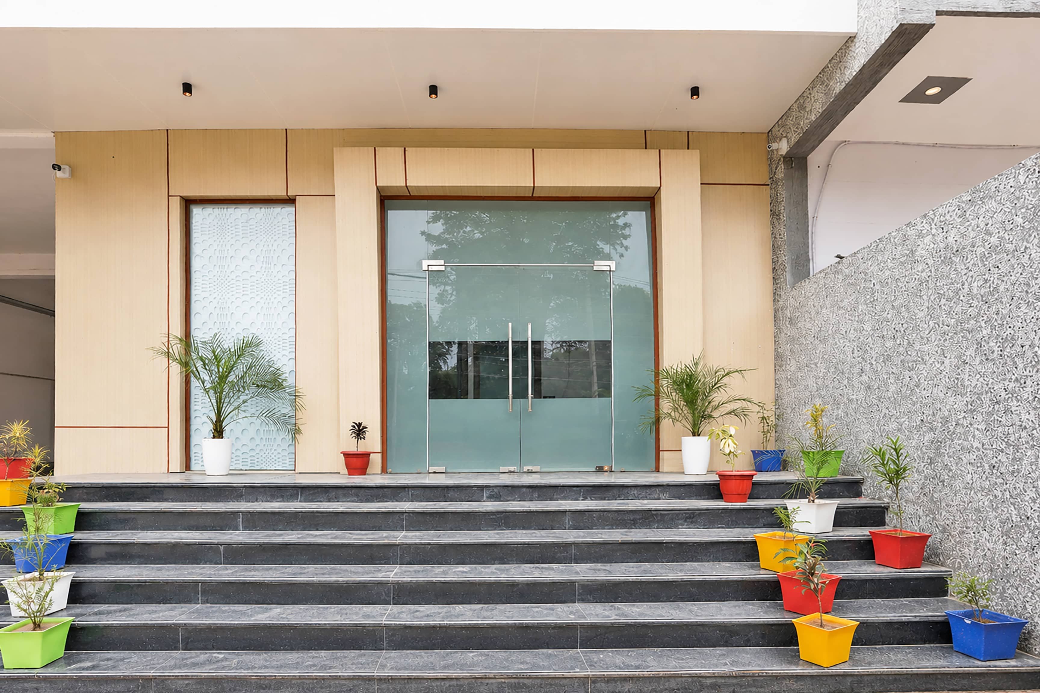 A building entrance with a glass door, steps leading up to it, and potted plants on the steps.
