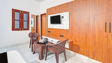 Quarto moderno com guarda-roupa de madeira, televisão fixada em parede de mármore, mesa de jantar com cadeiras e espaço para café.