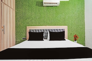 Un dormitorio con cama, cabecera, aire acondicionado de pared y una pequeña planta en maceta.
