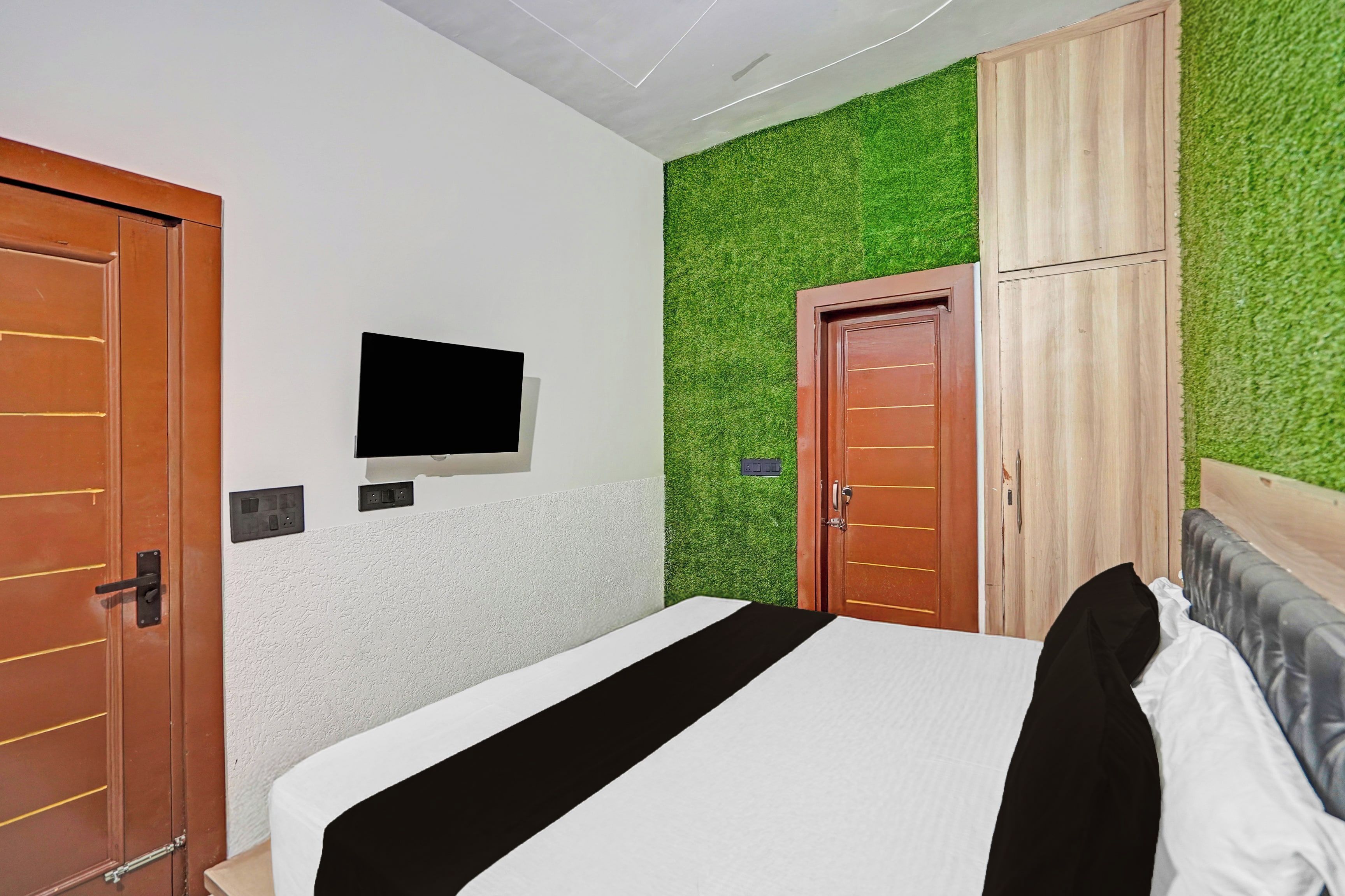 A hotel room with a bed, a television mounted on the wall, and a wardrobe.