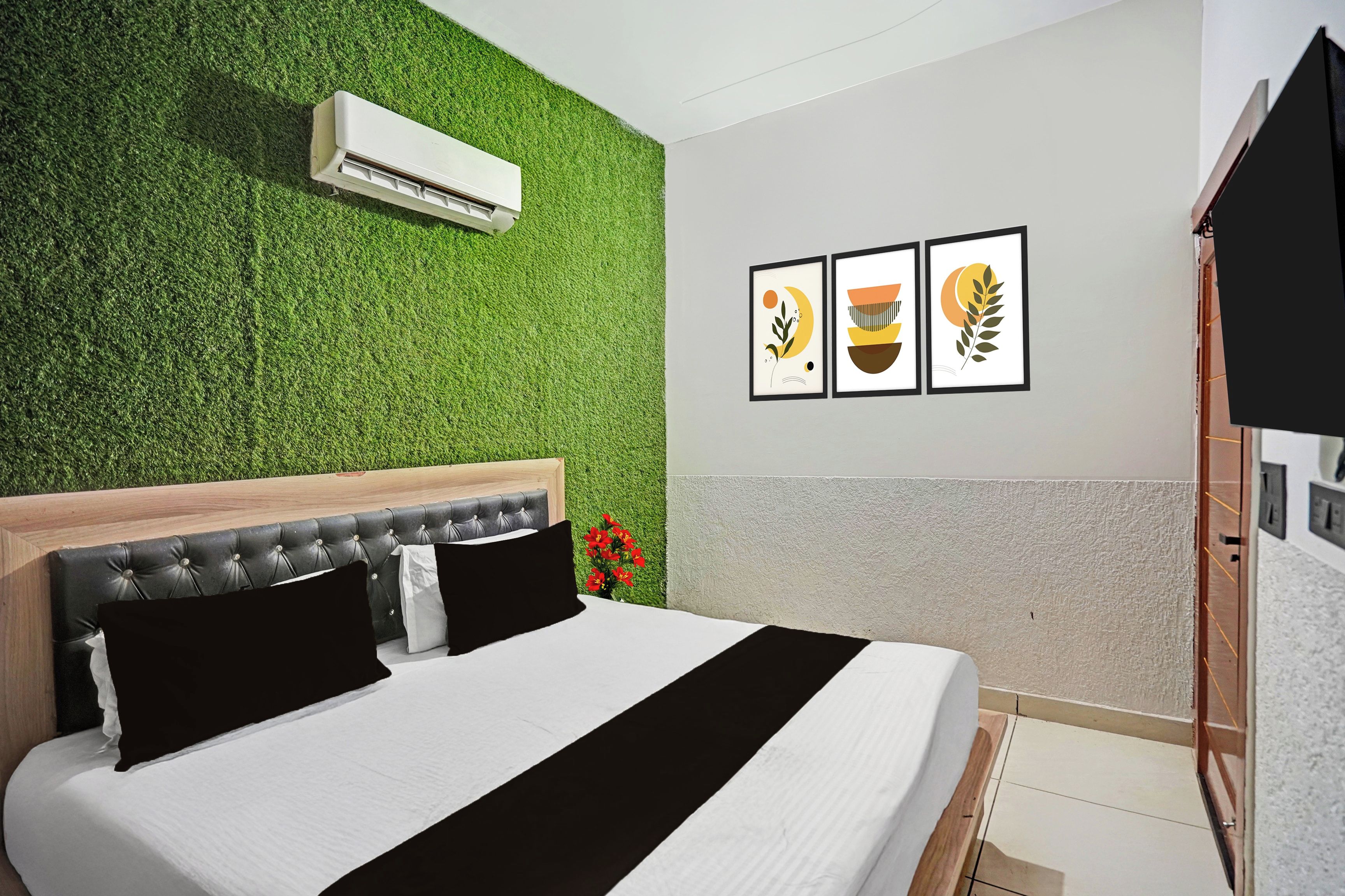 A hotel room with a green wall, a bed with black and white bedding, and three framed pictures on the wall.