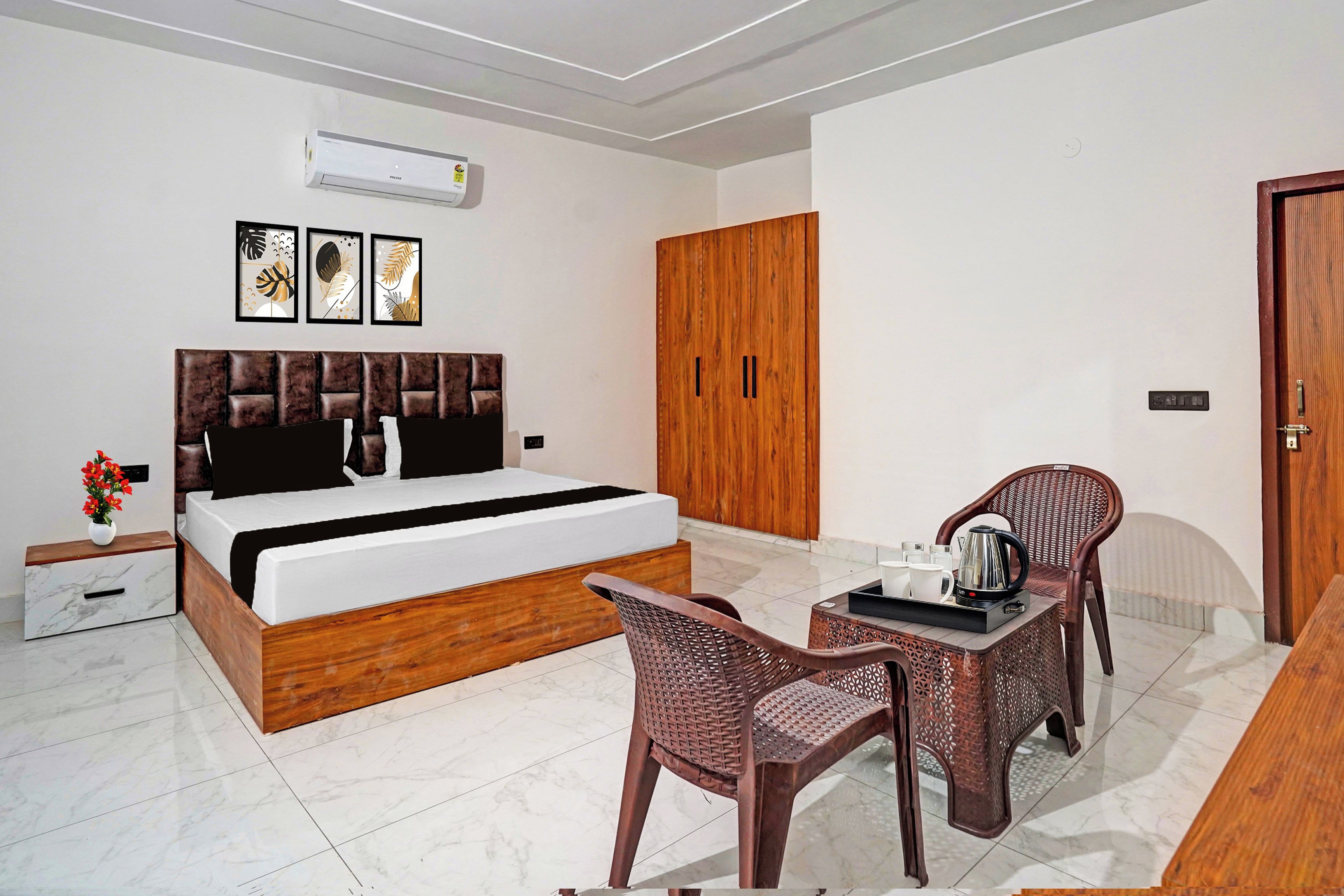 A hotel room with a bed, a wooden wardrobe, a small table with a kettle, and a wicker chair.