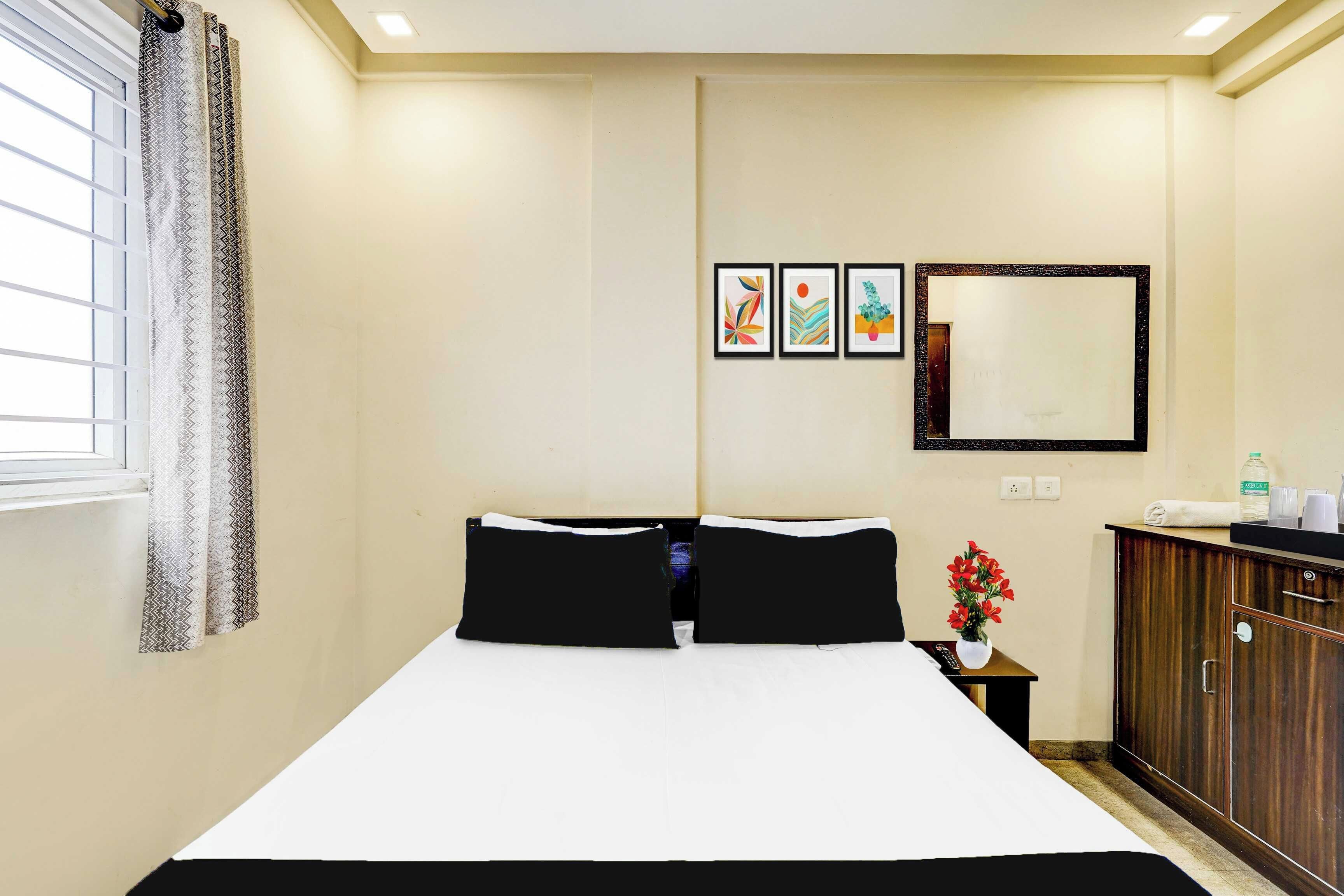 Habitación de hotel con cama, mesita de noche, espejo y ventana con cortinas.