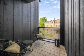 Ein Balkon mit Blick auf Gebäude, ein Stuhl, ein kleiner Tisch und ein Lautsprecher.