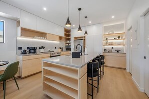A modern kitchen with a central island, bar stools, and built-in appliances. - New 3-Story Luxury Stay by City Park & Aggieville (Manhattan)