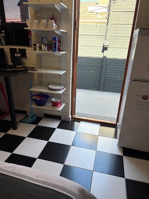 A kitchen with a black and white checkered floor, a refrigerator, and shelves with various kitchen items. - The Cola Cabana (Cape Town)